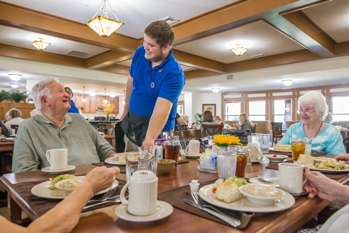 Seniors enjoy a meal with attentive staff in dining area.