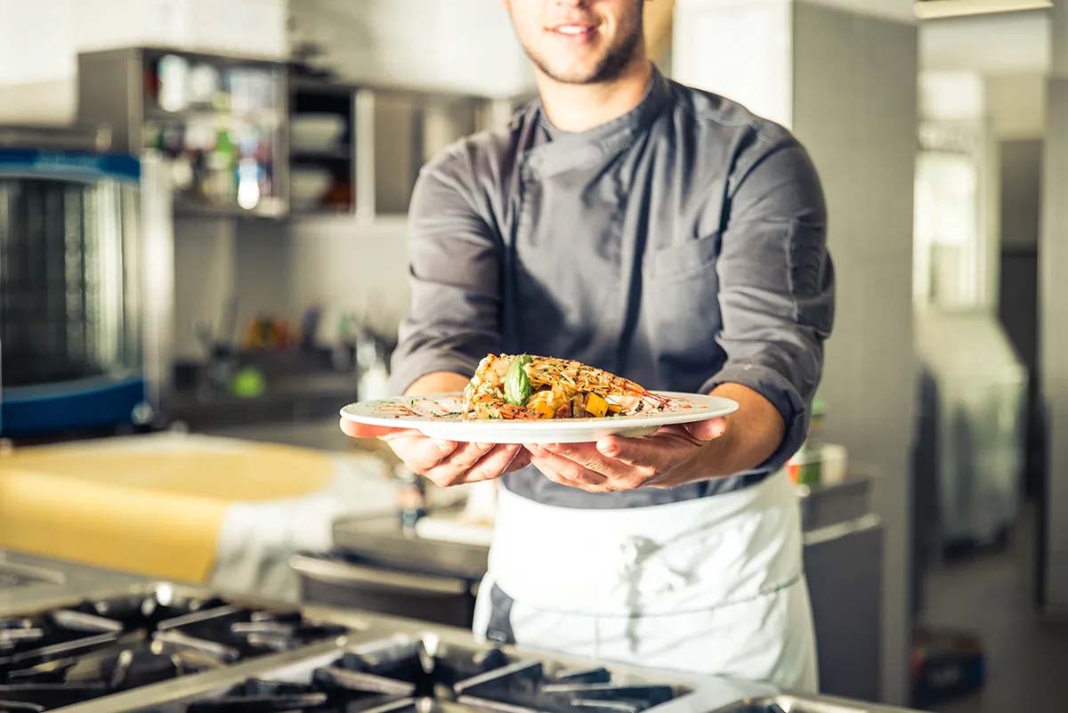 Chef presenting a beautifully plated dish in a kitchen.